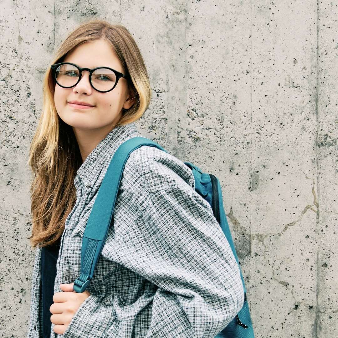 En teenager står med sin skoletaske på op ad en betonmur og smiler til kameraet.